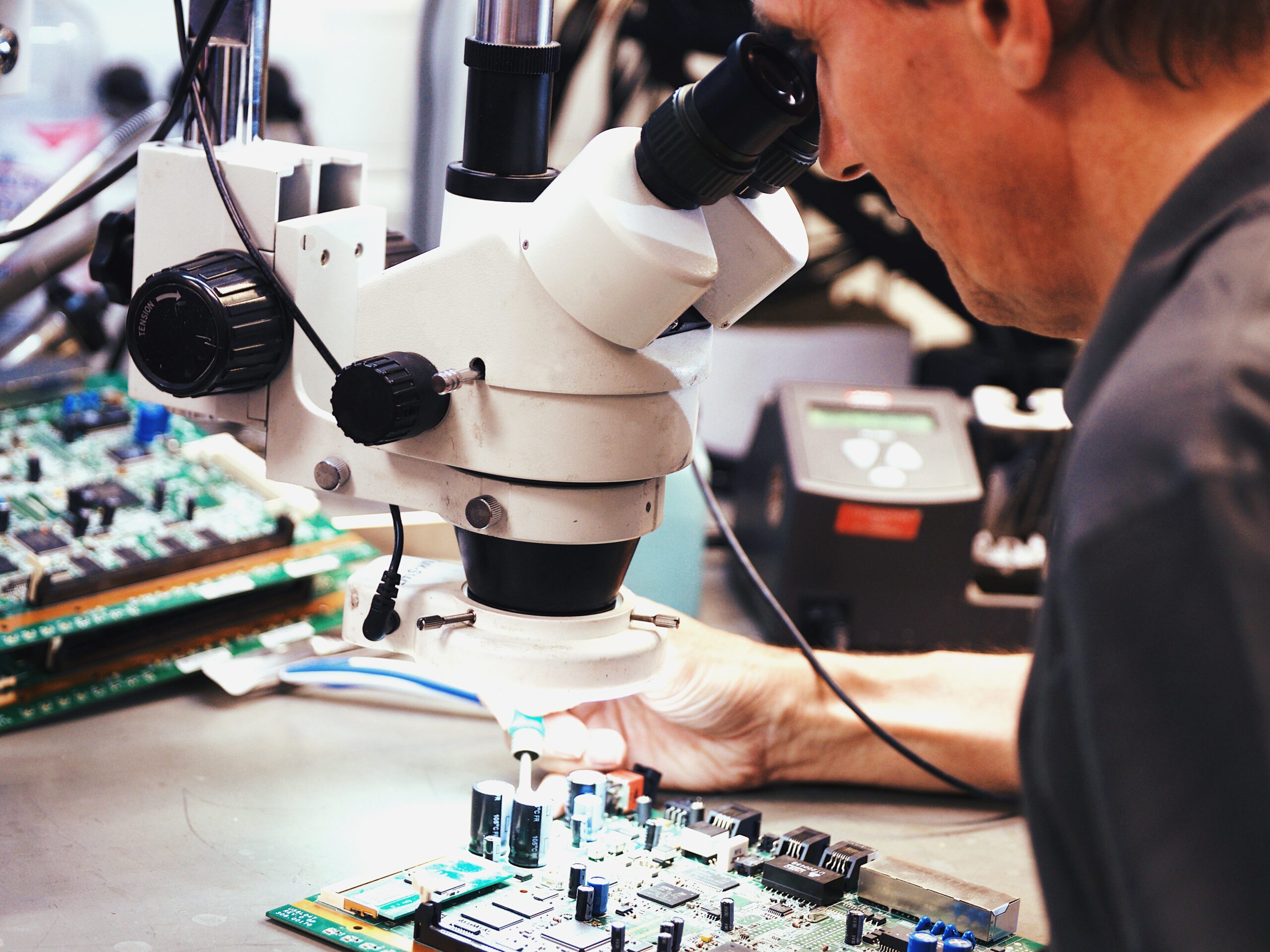 Technicien ENS réparant une carte de circuit imprimé sous un microscope pour Cisco Repair Services France